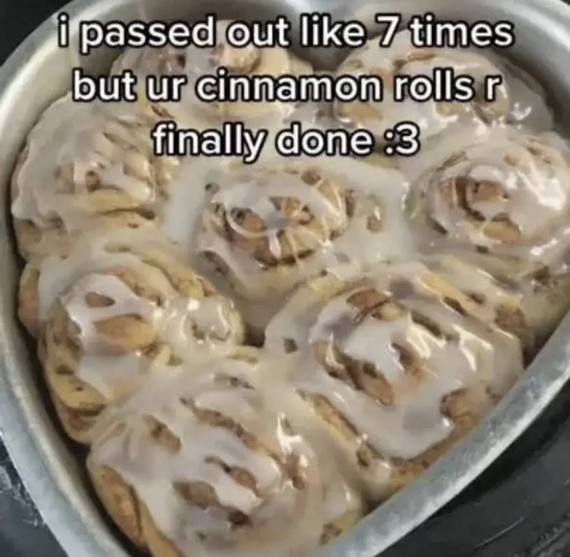 the caption "i passed out like 7 times but ur cinnamon rolls r finally done :3" on a picture of a heart shaped tray baking tray with cinnamon rolls with white icing