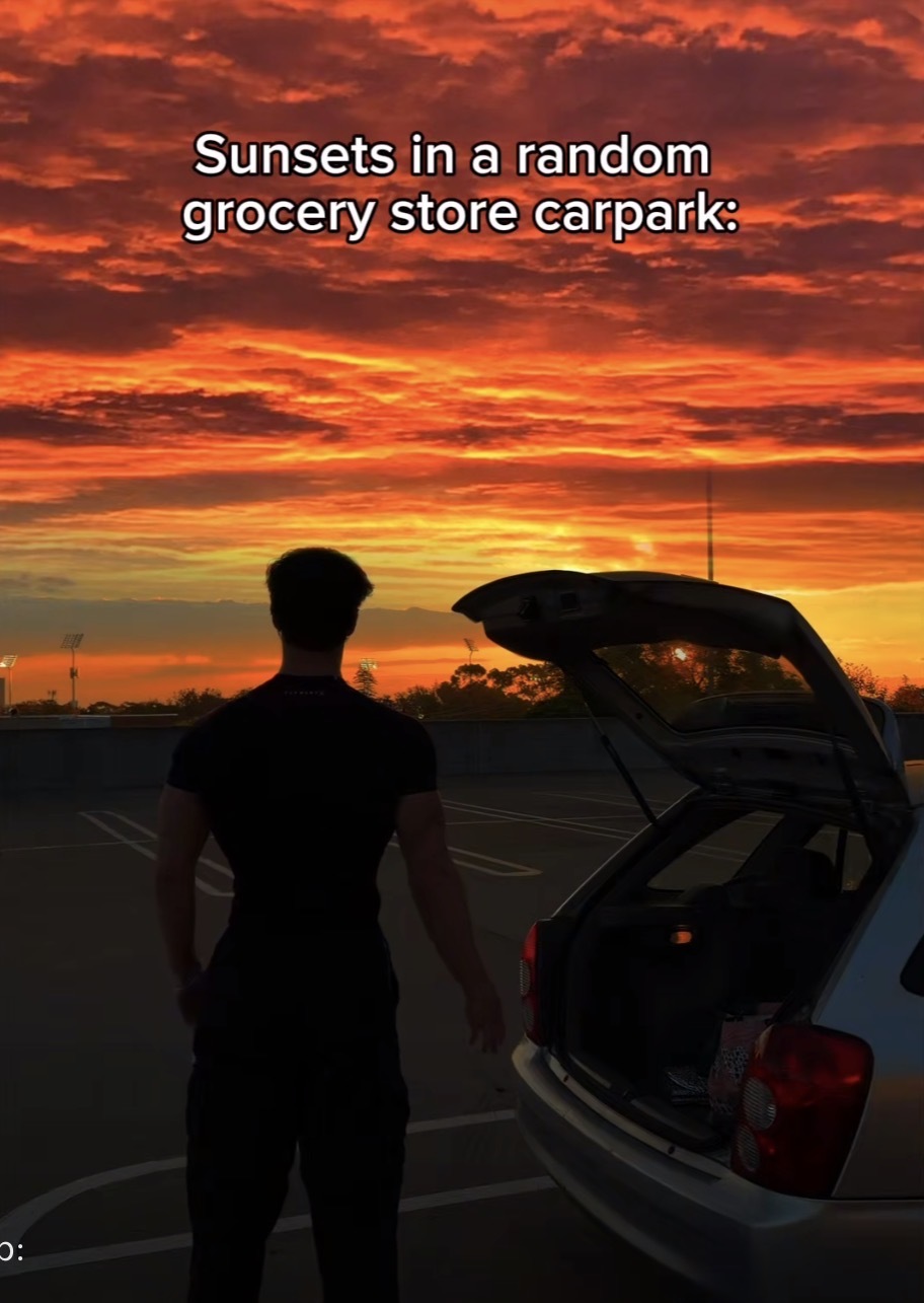 A stunning orange and red sunset with a person standing next to their car with the caption, “Sunsets in a random grocery store carpark”