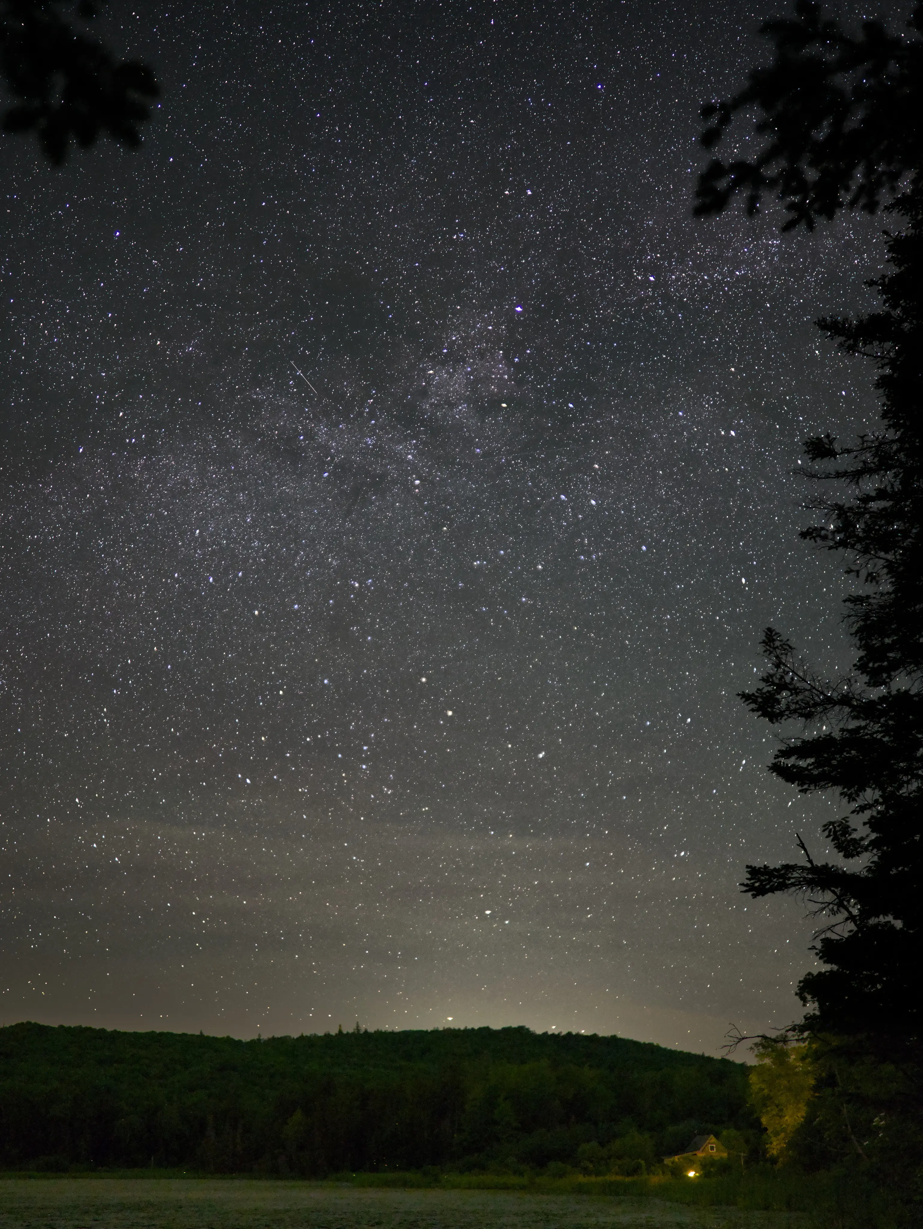 A small house sits on a pond beneath a vast array of stars.