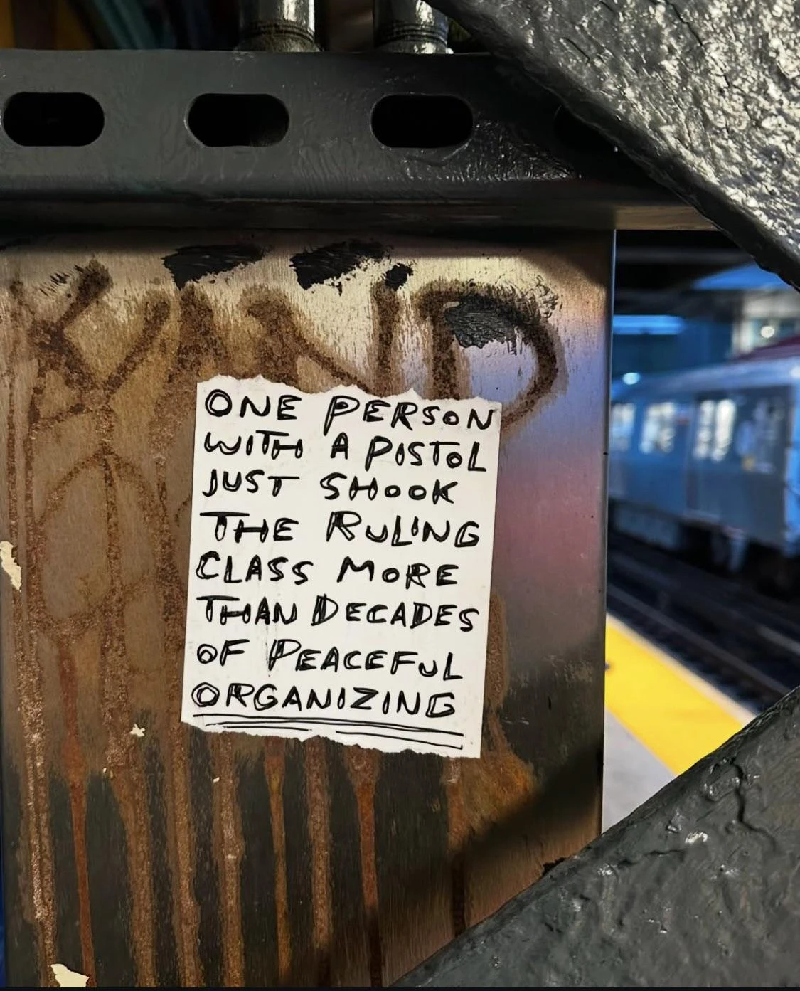 A sticker slapped in a NYC subway reads:  "One person with a pistol just shook the ruling class more than decades of peaceful organizing"